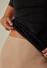Černý přiléhavý top, který se vytahuje, aby odkryl světle béžové elastické dno. Hladká textura s těsným střihem zvýrazňující pas.