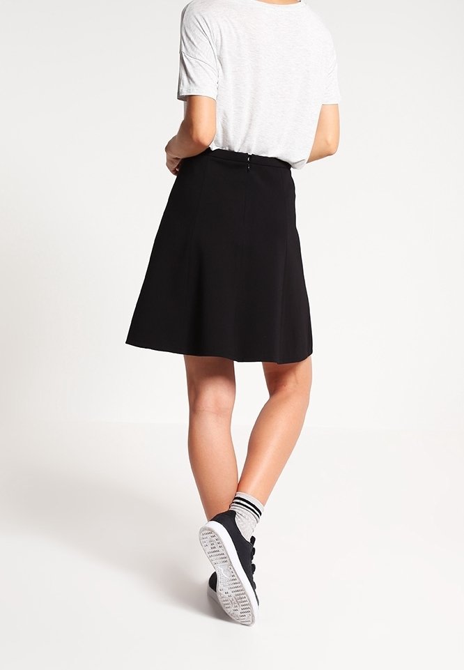 Jupe patineuse noire avec un design structuré, texture lisse et une fermeture éclair discrète à l'arrière. Assortie à un t-shirt gris et des baskets noires.