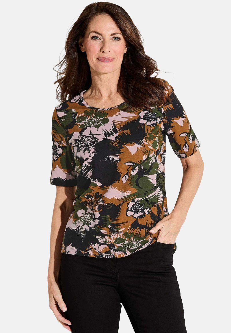 Bloemrijke t-shirt met korte mouwen, gekenmerkt door een multicolor patroon in bruin, groen en roze. Ronde halslijn en zachte stof. In combinatie met zwarte broek.