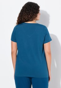 Teal kortepakken T-shirt met een ronde hals, zacht stof en een relaxte pasvorm, weergegeven vanuit de achterkant tegen een witte achtergrond.
