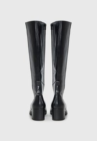 Black leather knee-high boots with a smooth texture, square heels, and visible zippers at the back, showcasing a minimalist design.