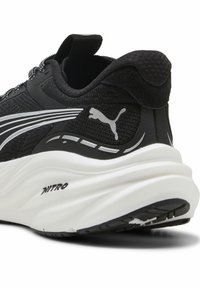 Scarpa sportiva nera con upper testurizzato, intersuola bianca ammortizzata e logo Puma. Presenta accenti grigi e un tallone rinforzato.