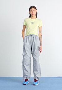 Tricou verde deschis cu logo-ul Nike, împreună cu o pereche de pantaloni cargo gri cu talie elastică și buzunare, completați cu adidași albaștri și roșii.