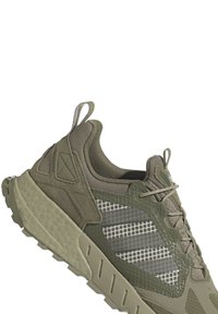 Olivgrön träningssko med mesh- och mockamaterial, texturerad gummisula, unika rutmönster på detaljerna och dragögla vid hälen.