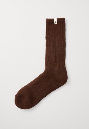 Brune strikkede sokker med ribbet tekstur, med en logo merkelapp på toppen og avrundet tå. Laget av mykt, varmt materiale.