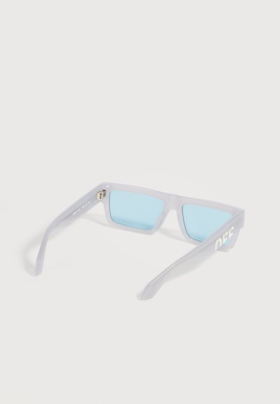 Lunettes de soleil rectangulaires avec montures blanches translucides et verres bleu clair, placées face vers le bas montrant les charnières intérieures et les branches latérales.