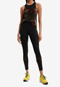 Mustat urheiluleggingsit, joissa on kukkaverkkokoristeet, ja musta toppi, joka sopii yhteen. Mallilla on päällään kirkkaankeltaiset lenkkarit.