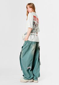 Camiseta de gran tamaño de color gris claro con estampado gráfico en la espalda, combinada con jeans de pierna ancha en azul desteñido y zapatos plataforma gruesos color blanco hueso.