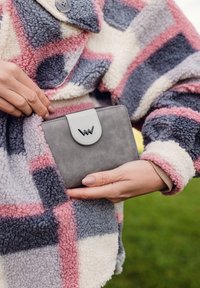 Gray wallet with a white flap and logo, partially tucked into a multicolored, fuzzy patterned coat featuring pink, gray, and white tones.