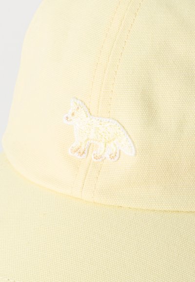 Hele kollane riidest nokamüts, mille esipaneelil on tikkitud rebane silueti logo, nähtavate õmblustega ja tekstuurse materjaliga.