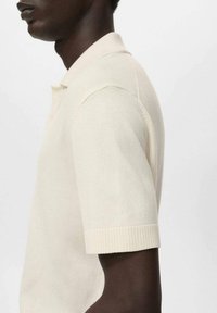 Beige neulepaita lyhyillä hihoilla, ribsikuvioidut hihansuut ja klassinen kaulus. Materiaali vaikuttaa pehmeältä ja siinä on sileä rakenne.