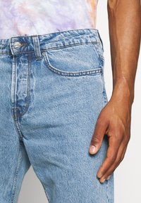 Jasnoniebieskie dżinsy z denimu z efektem sprania, z pięcioma kieszeniami, metalowym zapięciem na guzik i subtelnymi detalami przeszyć.