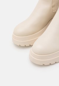Beige platform ankle boots made of smooth leather with a rounded toe, thick sole featuring a textured tread pattern, and minimal stitching details.