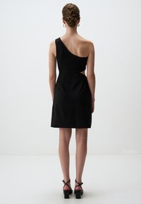 Schwarzes Kleid mit asymmetrischem, einseitigem Design und ausgestelltem Rock. Hergestellt aus glattem Stoff, mit Ausschnittdetails an der Taille.