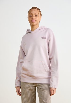 Jasnofioletowa bluza z kapturem wykonana z miękkiego materiału, z kieszenią kangurką, prążkowanymi mankietami i małym logo na piersi. Poniżej paski na spodniach.