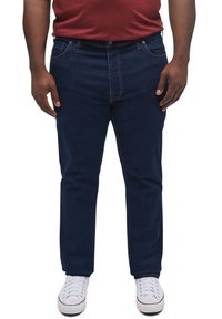 Jeanși din denim albastru închis cu un croi drept, având cusături portocalii, cinci buzunare și închidere cu nasture. Purtați cu adidași albi.