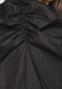 Tessuto nero con texture arricciata, caratterizzato da un design arricciato che crea profondità visiva. Materiale liscio e leggero.