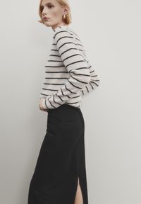 Un pull rayé de couleur crème clair avec des rayures noires, associé à une longue jupe noire dotée d'une fente sur le côté et d'une texture de tissu lisse.