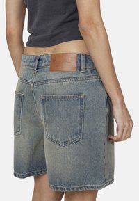 Shorts in denim di colore azzurro chiaro con un lavaggio sbiadito, dotati di due tasche posteriori e un'etichetta in pelle marrone sulla vita posteriore.