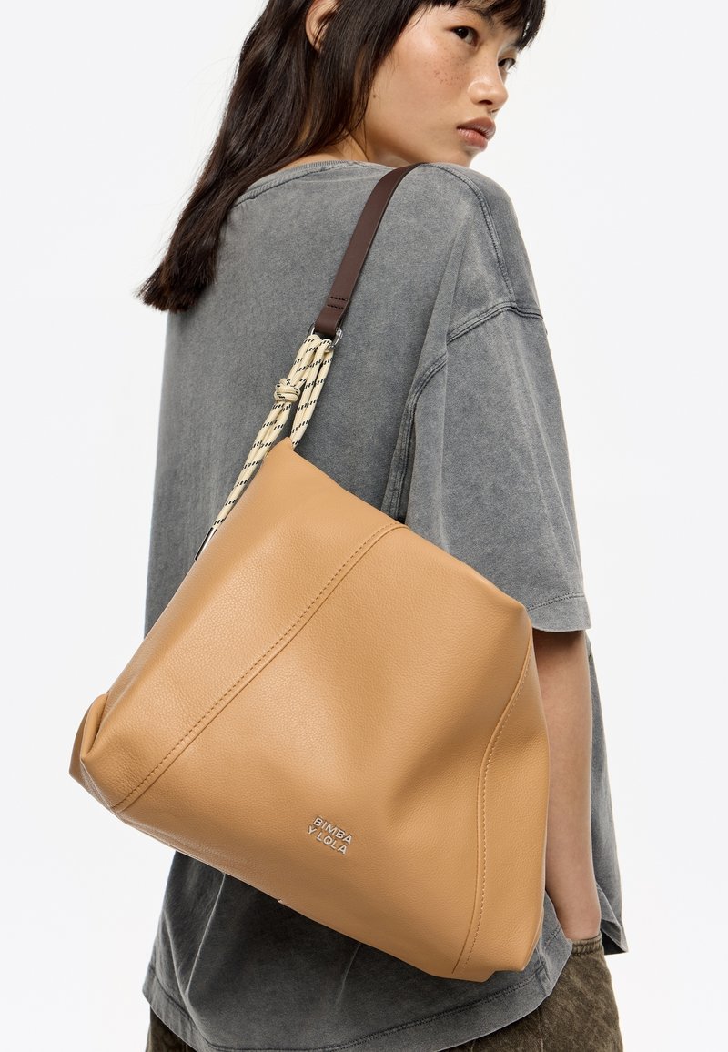 Borsa a spalla in pelle tannata con un design morbido. Presenta una tracolla decorativa intrecciata e un accento del logo argentato. Texture morbida.