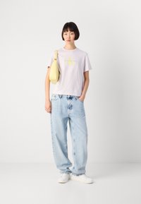 Lys lilla bomullst-skjorte med gult grafisk logo, kombinert med løse lyseblå denimjeans og hvite joggesko, akkompagnert av en gul crossover-veske.