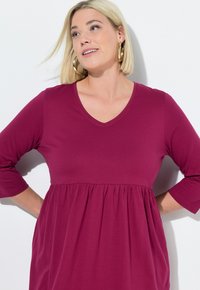 Šaty s výstřihem do V a tříčtvrtečními rukávy v hluboké magentové barvě, s přiléhavým korzetem a nařaseným pasem. Měkká směs bavlny.