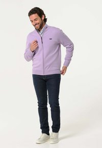 Lichtpaarse zip-up trui met hoge kraag, geribde manchetten en onderrand. Draag het met donkerblauwe jeans en witte sneakers.