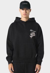 Zwarte katoenen hoodie met een capuchon, een voorzak en een gemarkeerde afbeelding op de linkerborst; heeft ribbelboorden en een elastische tailleband.