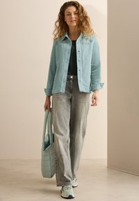 Giacca di denim azzurro chiaro con bottoni, top nero, jeans grigi e sneakers azzurro chiaro. Porta una borsa a tracolla trapuntata azzurro chiaro.