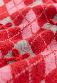 Vlněná tkanina s argyle vzorem v červené, růžové a šedé barvě, doplněná malými červenými pletenými mašlemi a jemnou, chlupatou texturou.