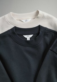 To sweatshirts stablet, en cremefarvet og en navyblå. Begge har ribstrikkede halsudskæringer og mærker med teksten "THE SET" i størrelse M. Blød stoftekstur.