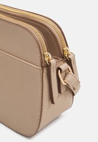 Beige crossbody taske lavet af tekstureret læder, med to gyldne lynlåse og en aftagelig rem. Glatte kanter og minimalistisk design.
