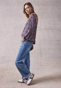 Camicia a maniche lunghe con un motivo multicolore, abbinata a jeans azzurri e sneaker bianche con strisce nere.