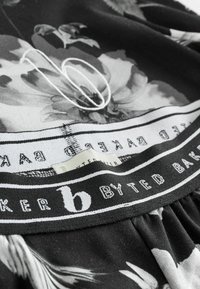 Kvetinový vzorovaný textil v čierno-bielom vyhotovení, s čiernym elastickým pásom s nápisom a viditeľnou etiketou pod ním.