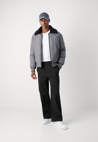 Doudoune grise avec un col en polaire noir, associée à un t-shirt blanc et un pantalon noir. Comprend une casquette de baseball grise et des baskets blanches.