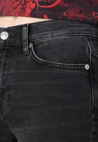 Jeans de mezclilla negra con una textura suave, que presentan un bolsillo frontal, herrajes plateados y un ligero desteñido en el color a lo largo de la pierna.
