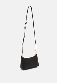 Sac à bandoulière en cuir noir avec fermeture éclair dorée et sangle longue réglable, présenté suspendu contre un fond clair uni.