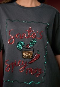 Grijs T-shirt met korte mouwen met het ontwerp "Santa's Spicy Mez" in rode en groene pailletten, met een cocktailglas, chilipeper en feestelijke details.