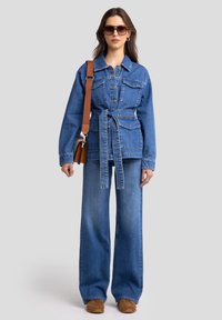 Jeans jakna z obsegom pasu, velikimi žepi in ovratnikom. V kombinaciji z širokimi jeans hlačami in rjavimi čevlji. Očala kot dodatek.