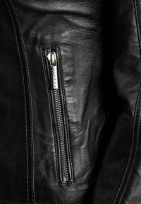 Zwarte leren jas met een ritszak met zilverkleurige hardware, getextureerd oppervlak en gladde afwerking. Close-up van het stofdetail.