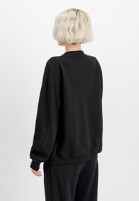 Crni oversized dukserica s rebrastim ovratnikom, dugim rukavima i opuštenim krojem. Mekana tkanina s minimalnim detaljima šava.