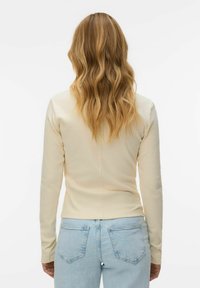 Kreemjas, pika varrukaga, keha järgiva lõikega särk, millel on sile tekstuur ja seljal keskmine õmblus. Sobitatud helesiniste teksapükstega.