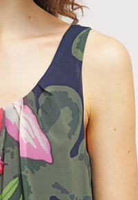 Ärmlös topp med blommönster som har en marinblå axelparti, mjuk grön tyg med rosa och vita blommönster, och en lätt textur.