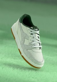 White sneaker with green accents, textured gray suede, and perforated detailing. Features laces and a gum rubber sole for traction.