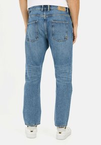 Jasnoniebieskie dżinsy o prostym kroju, pięć kieszeni i skórzana naszywka na pasku. Noszone z białymi sneakersami.