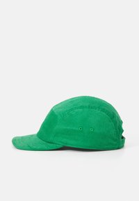 Green corduroy cap with a structured peak, textured fabric, and ventilation grommets. Features a rounded crown and flat bill.