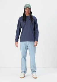 Navy long-sleeve shirt paired with light blue jeans and white sneakers featuring red accents. The person is wearing a green cap.