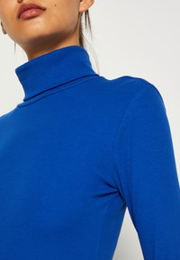 Blå ribbet turtleneck med lange ermer. Har en høy krage og en tettsittende design som viser en jevn tekstur og en livlig farge.