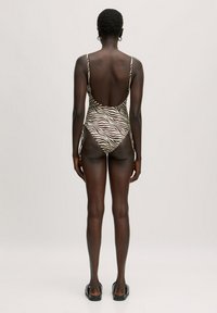Zebra-gepatroneerde badpak in neutrale tinten, met dunne bandjes en een lage rugontwerp. Gladde textuur en aansluitende pasvorm.