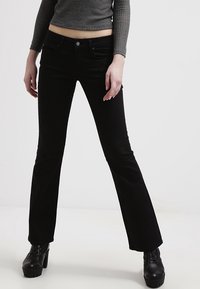 Jeans neri a zampa d'elefante in morbido tessuto, con chiusura a bottone e tasche frontali. Indossati con un top a maniche lunghe a costine e stivali con plateau.